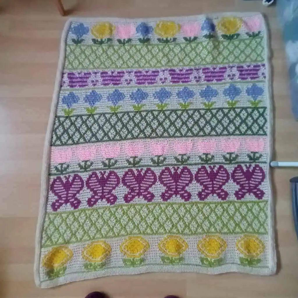 Knitted floral rug with colorful patterns and flowers in pink, yellow, purple, and green.