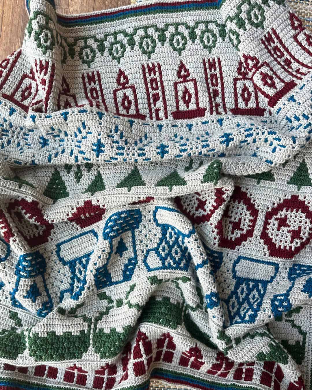 Mosaic crochet blanket featuring festive holiday motifs in red, green, blue, and white for Christmas.