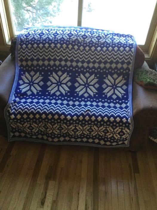 Handcrafted Nordic star mosaic crochet blanket in blue and white, draped over a sofa near a window.