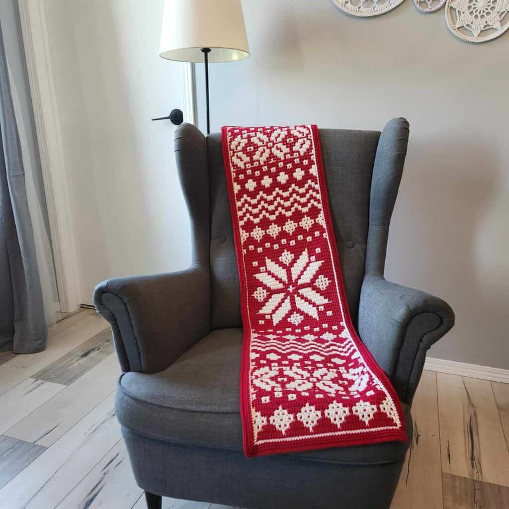 Nordic star mosaic crochet blanket draped over a gray armchair, showcasing intricate winter-inspired.