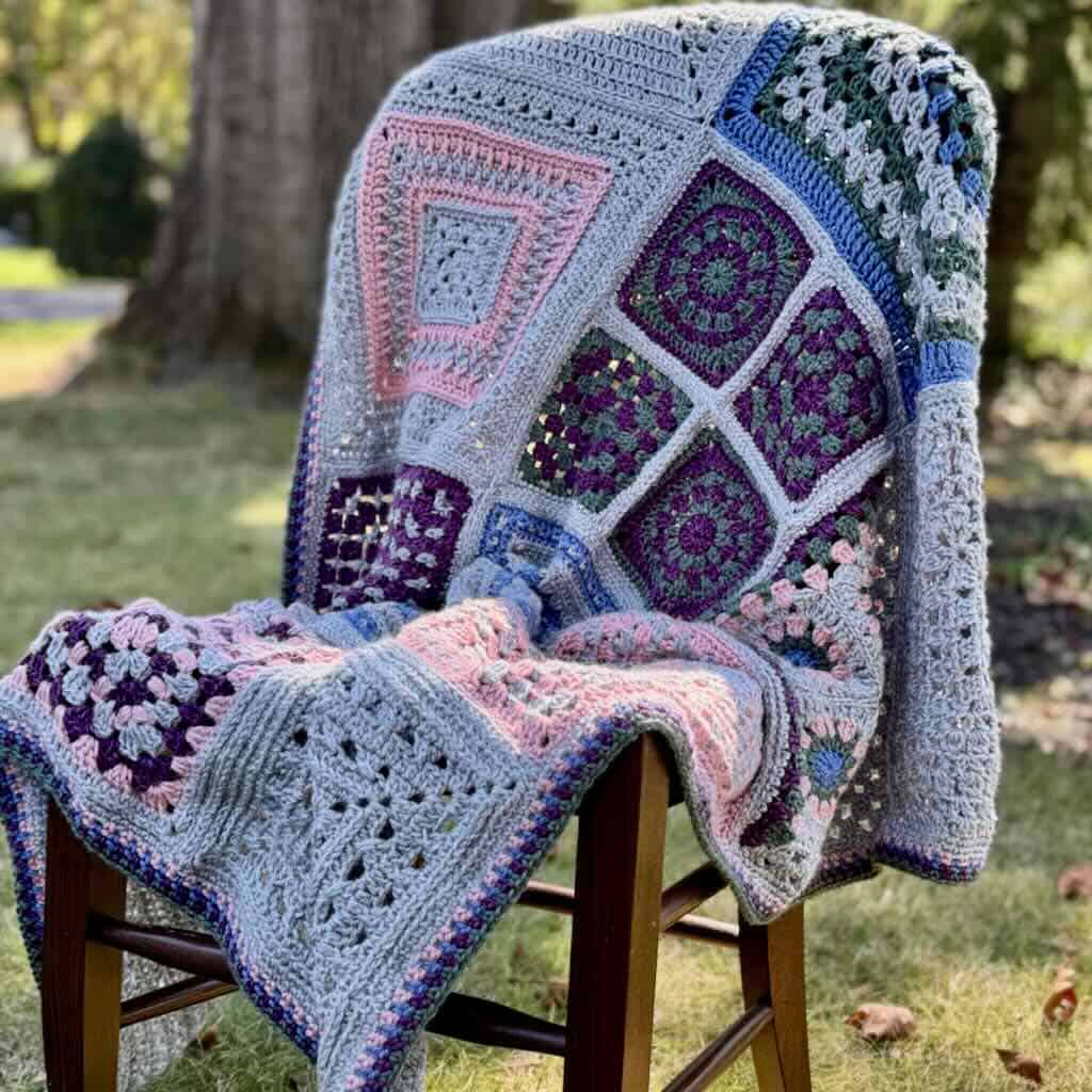 Colorful crochet granny square blanket with heart motifs draped over a wooden chair.