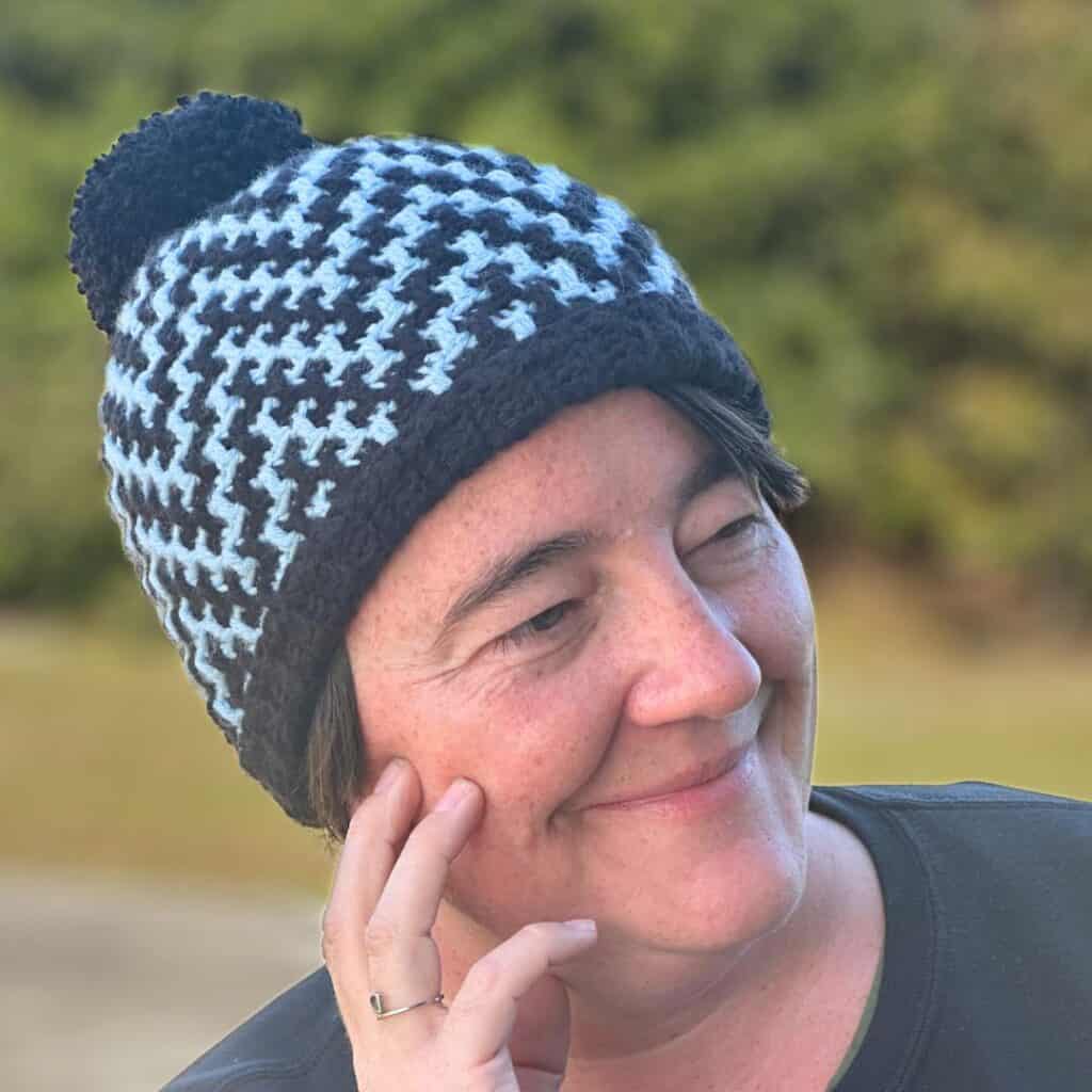 Woman wearing a blue and white houndstooth crochet hat outdoors.