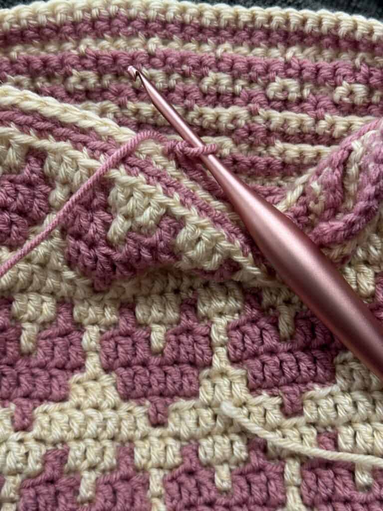Close-up of crochet mosaic hearts scarf with pink and cream yarns and crochet hook.