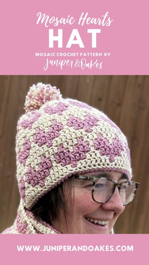 Up of a woman wearing a pink and cream mosaic hearts crochet hat with pom-pom, showcasing handmade w.