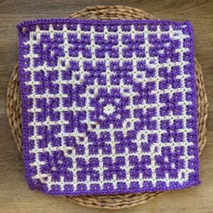 Crochet mosaic square featuring a dogwood flower pattern in purple and white.
