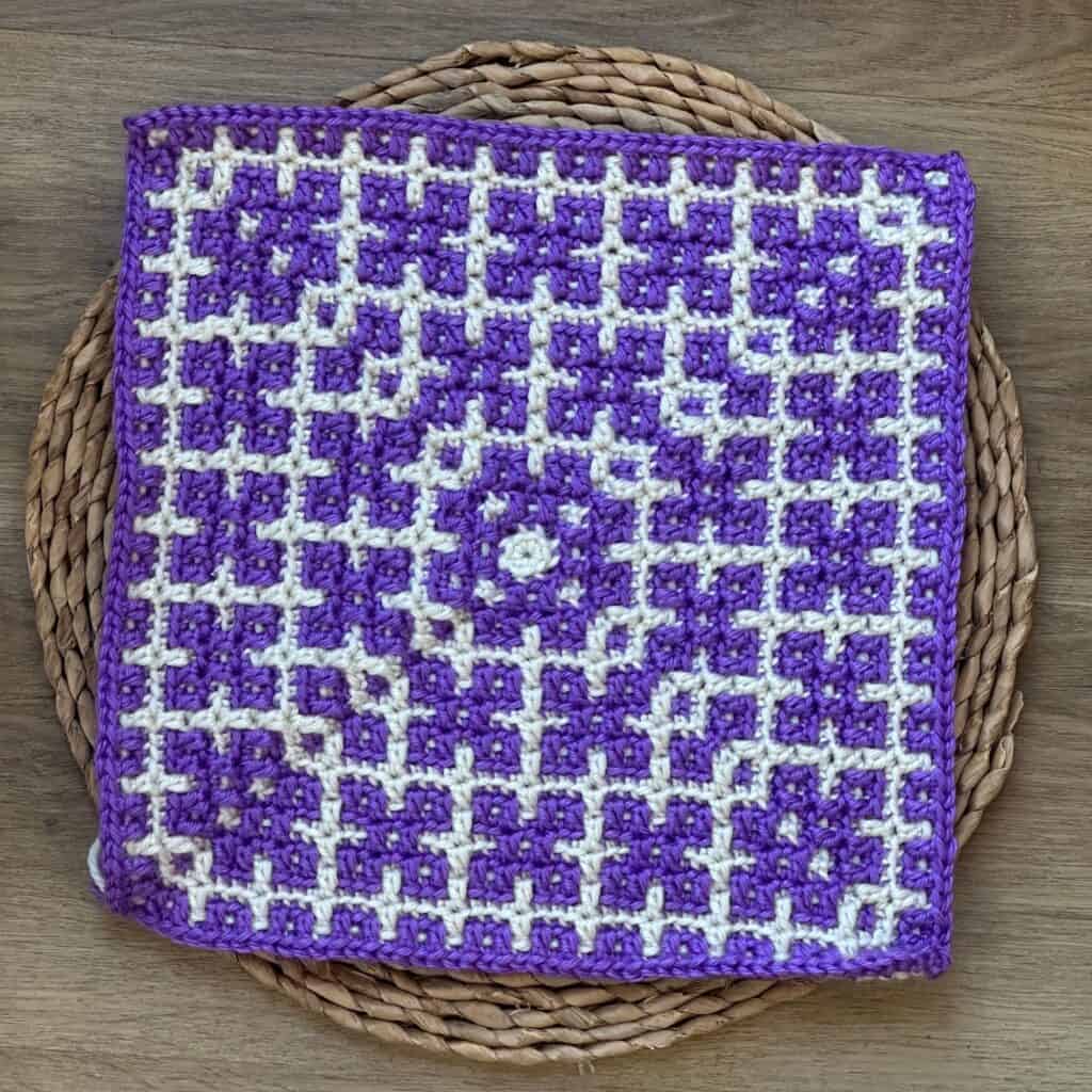 Crochet mosaic square featuring a dogwood flower pattern in purple and white.