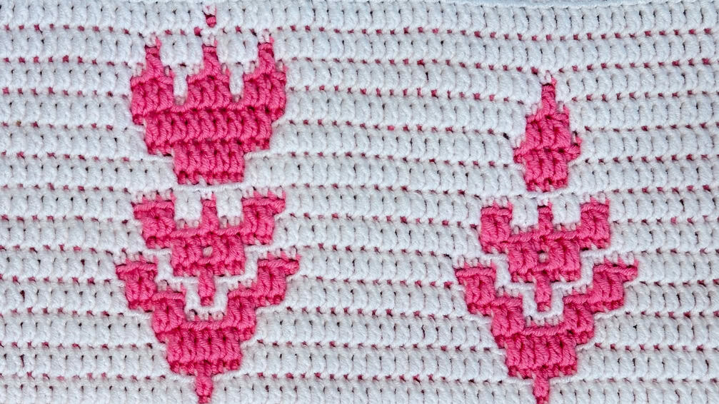 Close-up of pink and white crochet mosaic blanket strip with floral design.