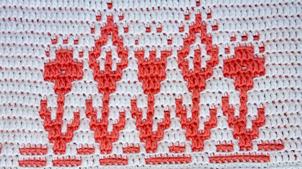 Close-up of a colorful crochet mosaic blanket strip with summery flowers in coral and white.