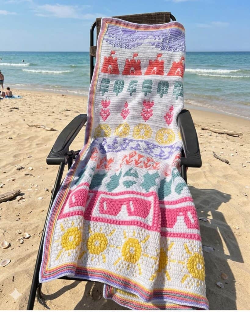The summer mosaic crochet blanket arranged on a lawn chair at the beach.