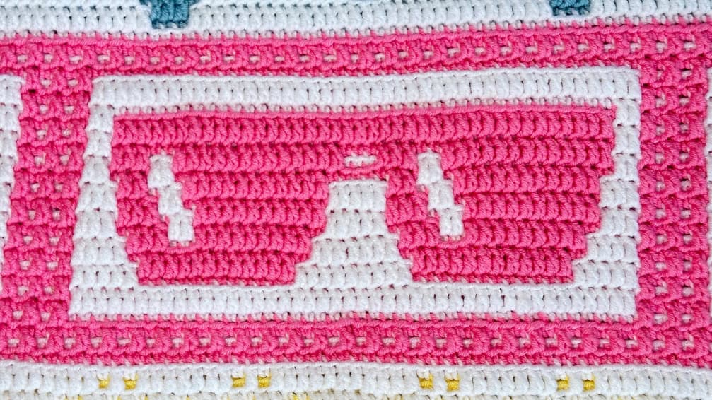 Bright pink and white crochet blanket with sunglasses design for summer.
