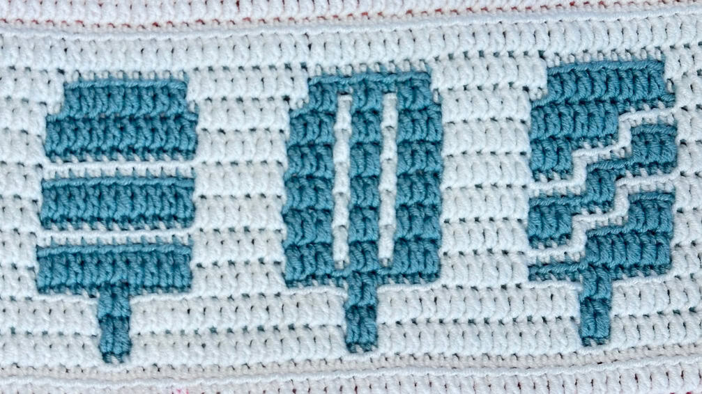 Close-up of a colorful mosaic crochet blanket strip with popsicle motif in blue and white.