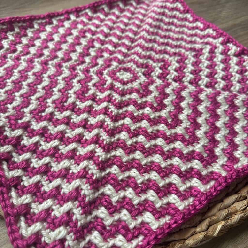 Close-up of a vibrant pink and white mosaic crochet square with ripple pattern.