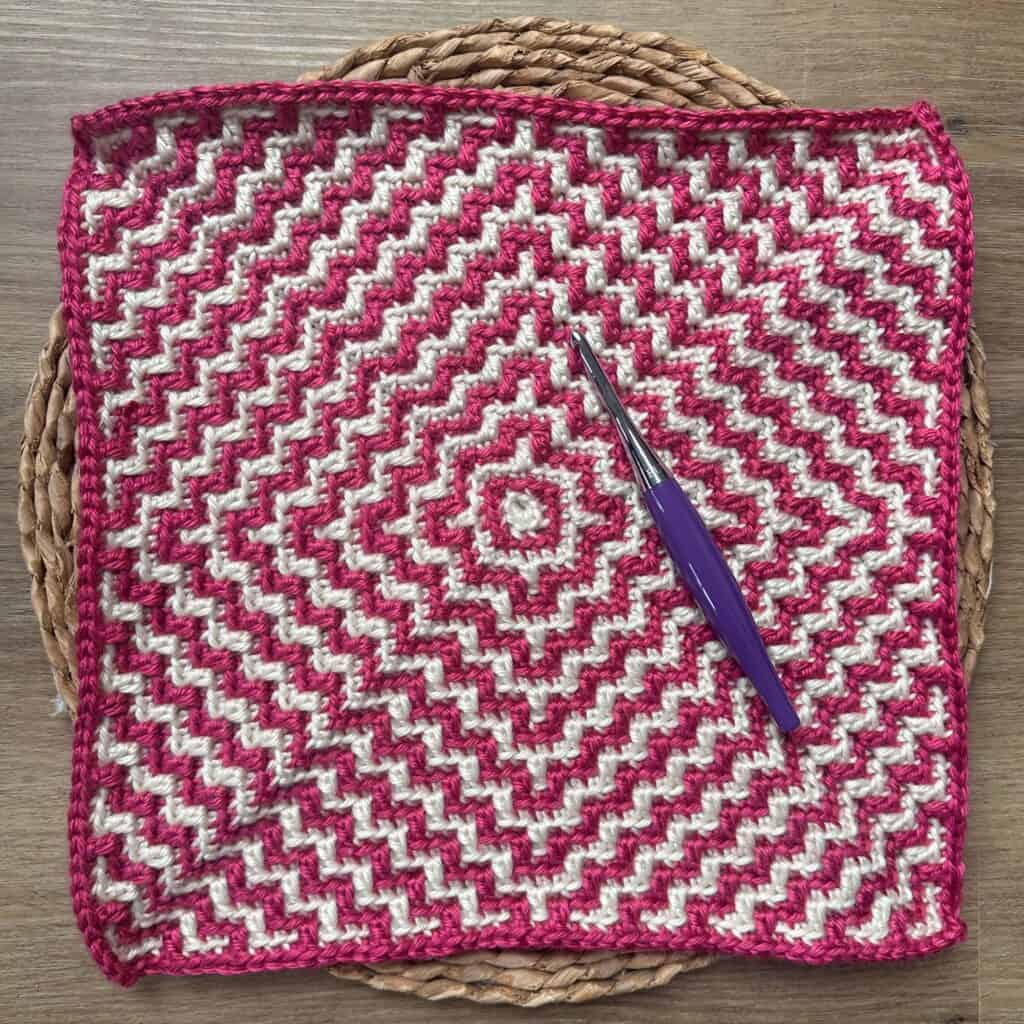 Colorful mosaic crochet square with pink and white rippling pattern.