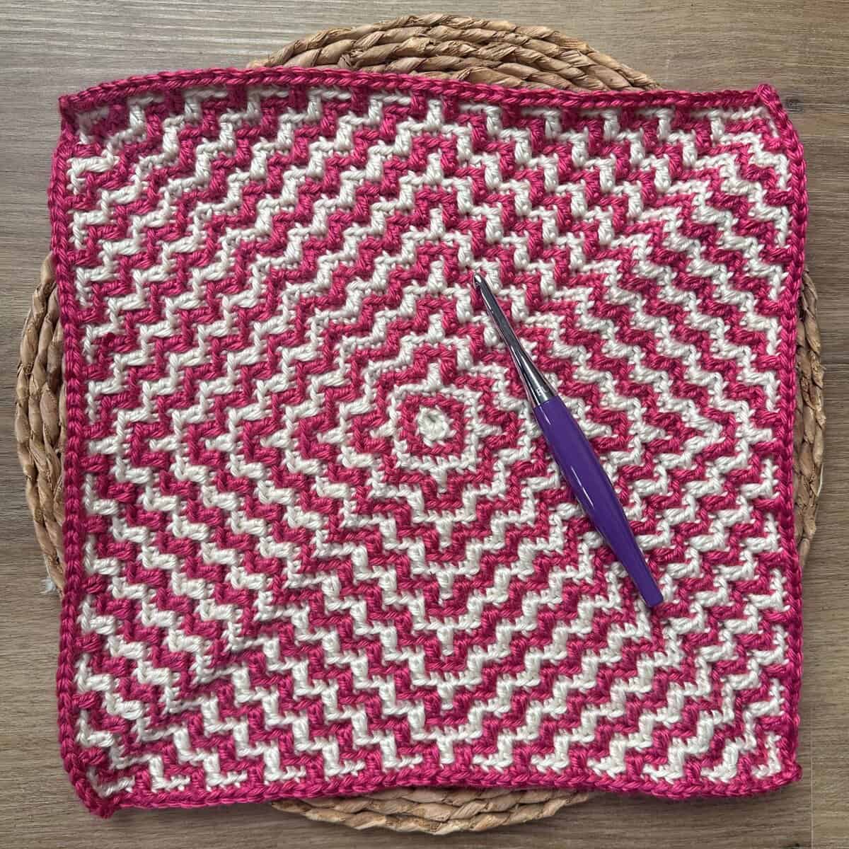 Colorful mosaic crochet square with pink and white rippling pattern.