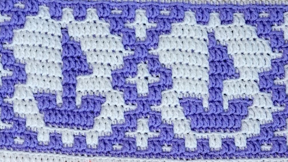 Close-up of a colorful crochet mosaic blanket strip with sailboat motif in purple and white.