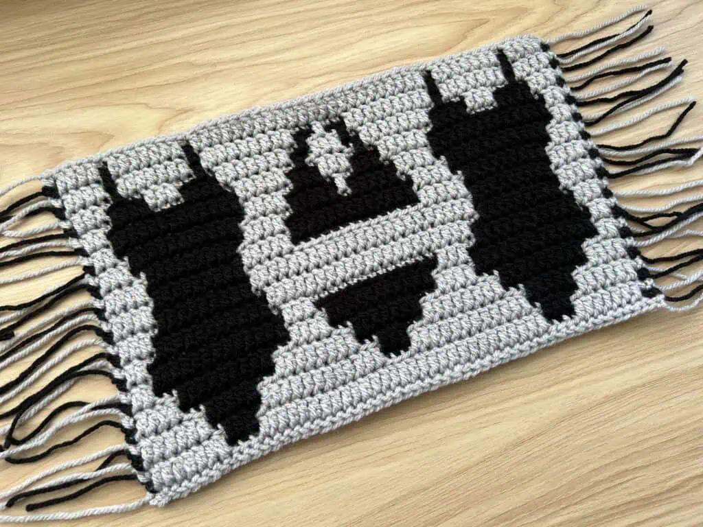 Black mosaic crochet swim suits design on a gray backdrop, laying on a wooden surface.