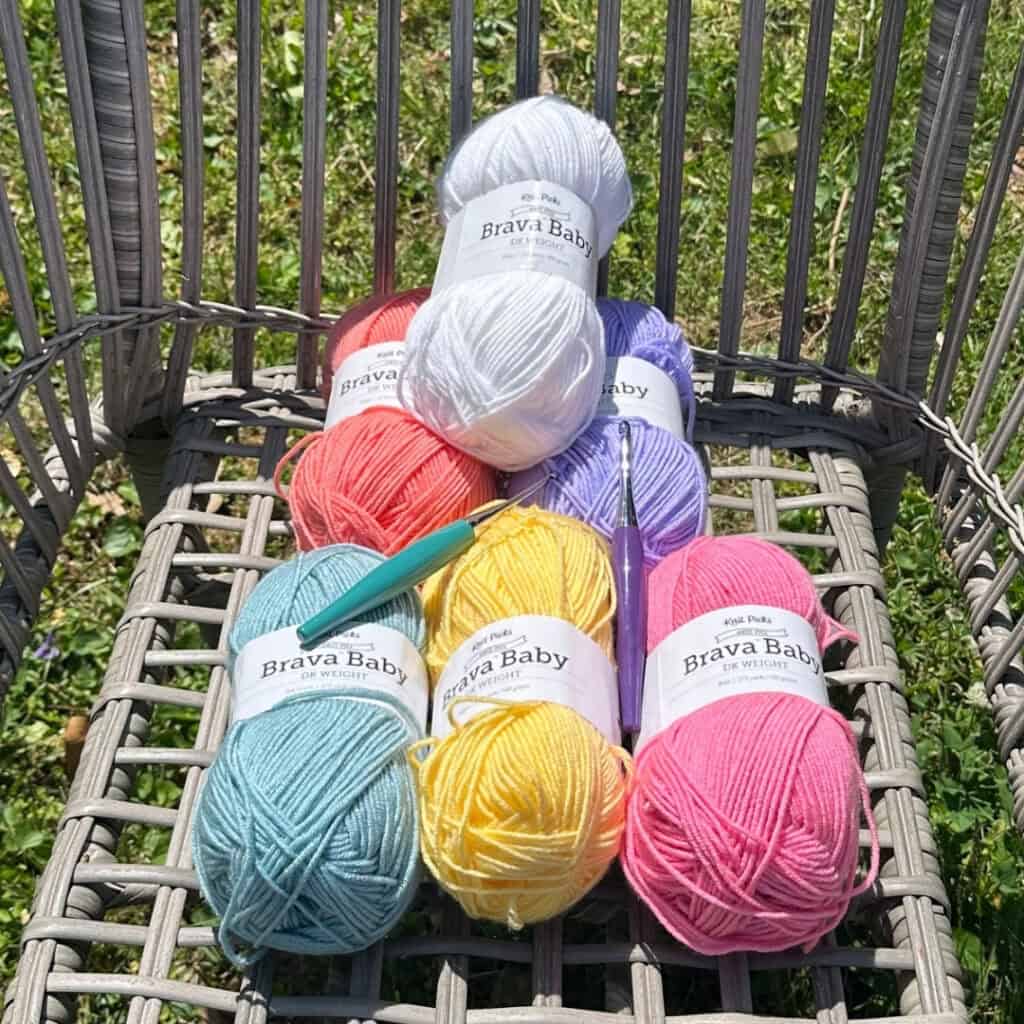 Brightly color yarn and hooks for the mosaic crochet summer blanket, arranged outside on a wicker chair