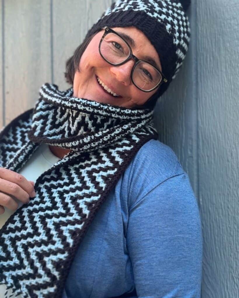 ZigZag mosaic crochet scarf in black and white, styled with a woman wearing glasses and a beanie. Pe.