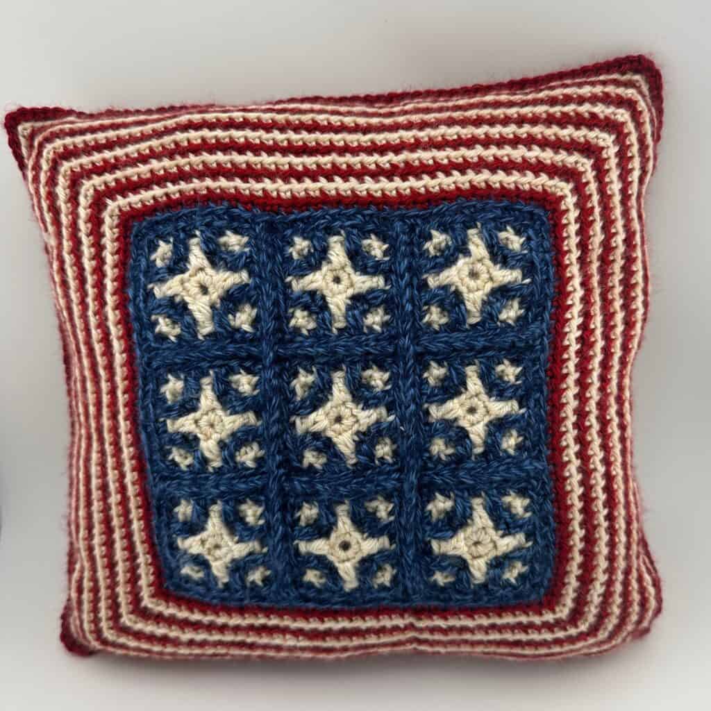 Patriotic crochet pillow with stars and stripes in red, white, and blue colors.