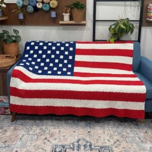 American flag c2c crochet blanket draped over a blue sofa in a cozy room.