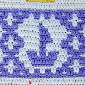 Close-up of a mosaic crochet sailboat pattern in white and purple yarn.