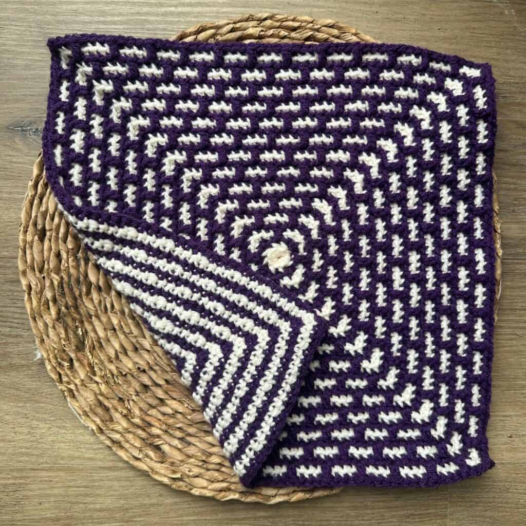 Purple and white woven textile with a geometric pattern, displayed on a round woven mat.