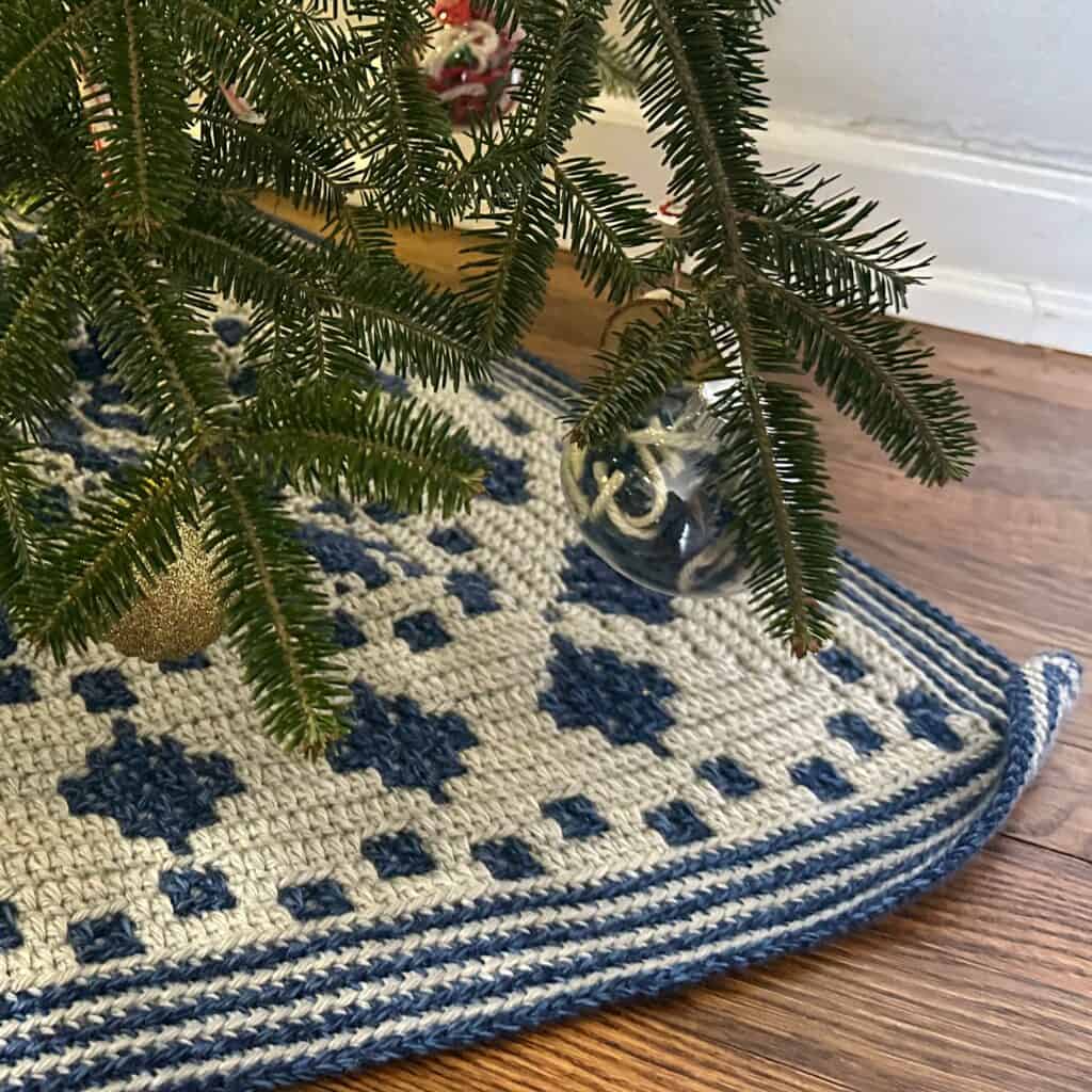 Close-up of a Christmas tree surrounded by a mosaic crochet Christmas tree skirt.