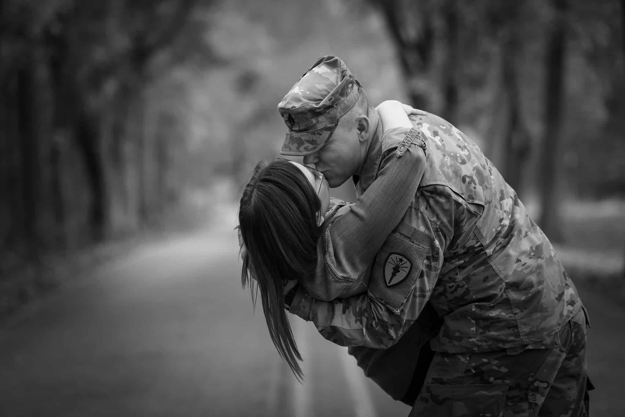 Army soldier dips and kisses woman in the road under fall trees