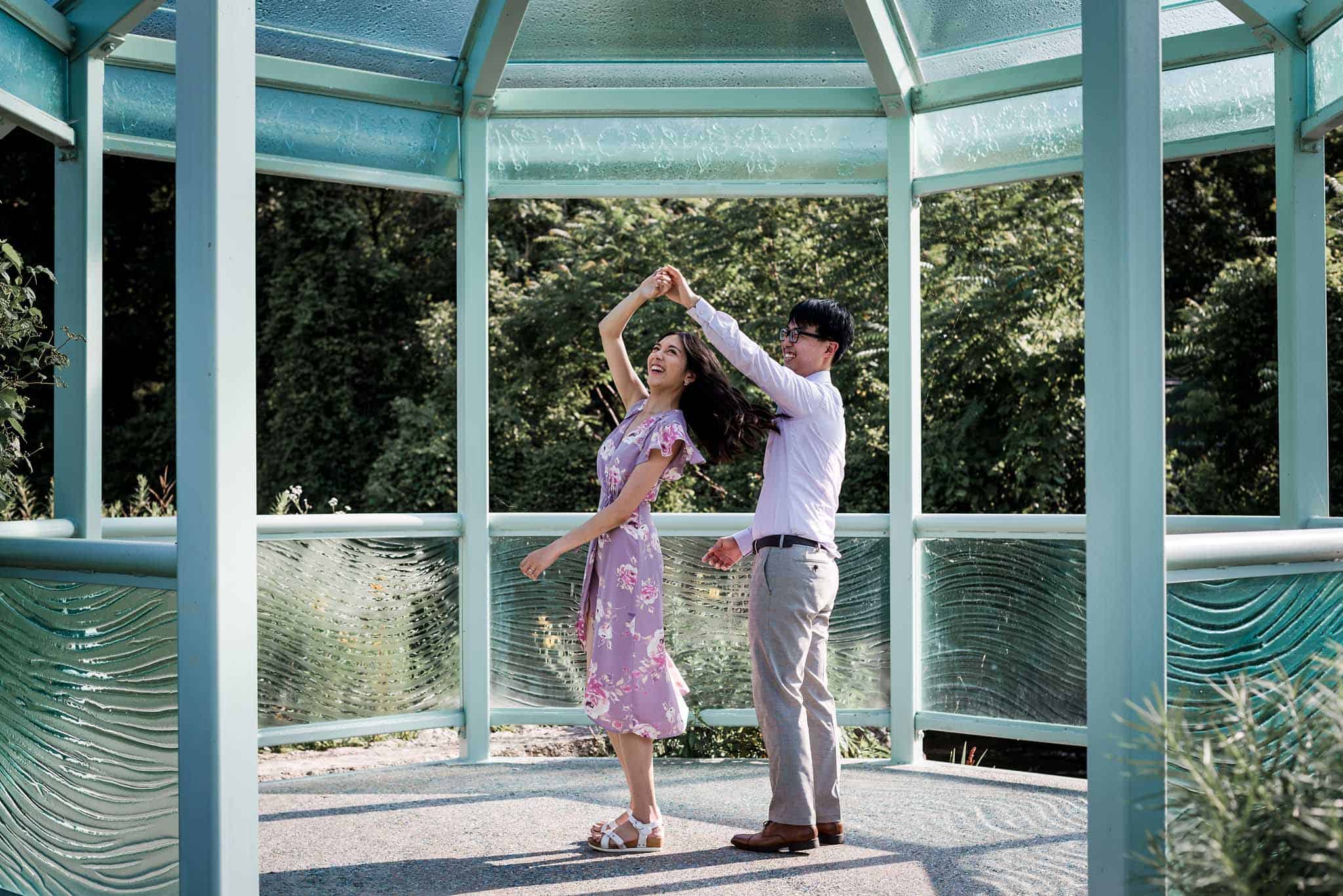 Young couple in lavender floral dress and lavender shirt dancing under teal pergola in botanical gardens