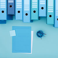 Blue office binders, notepad, and paperclip on blue background.