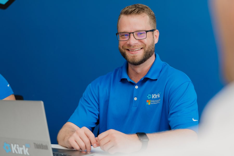 IT support specialist wearing Kirk IT uniform smiling at work.