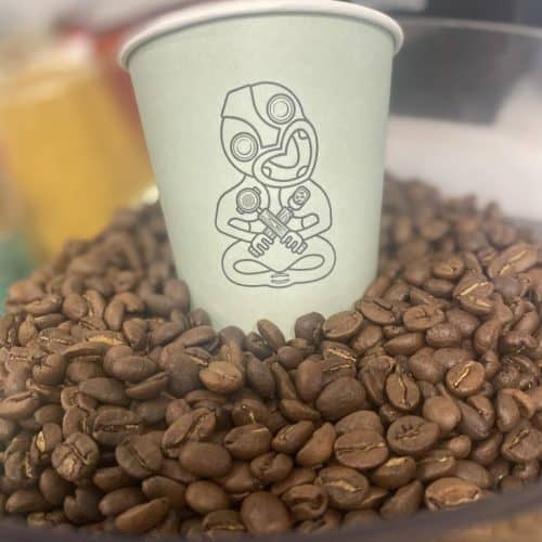 A latte cup with a unique cartoon design placed on a bed of roasted coffee beans at Knead Donuts.