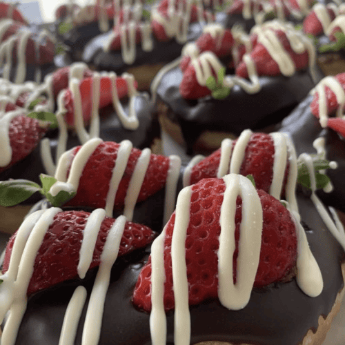 Delicious donuts topped with strawberries, chocolate glaze, and white chocolate drizzle, perfect for any treat craving.