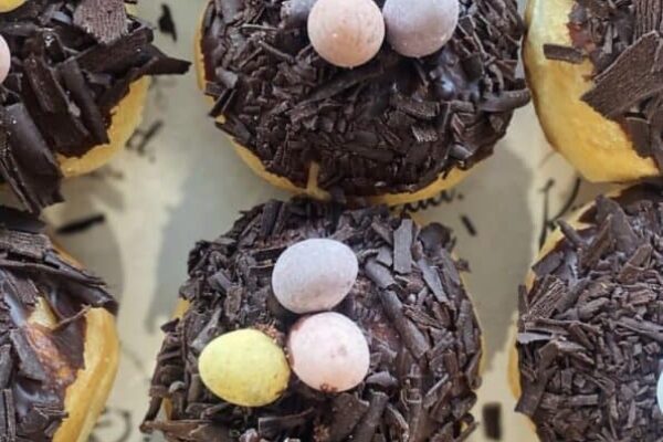 Delicious chocolate-covered donuts topped with pastel candy eggs, perfect for Easter treats.