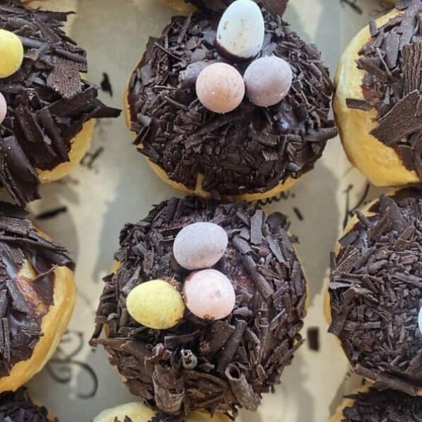 Delicious chocolate-covered donuts topped with pastel candy eggs, perfect for Easter treats.