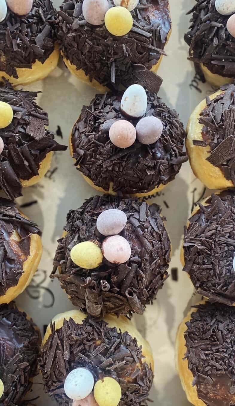 Delicious chocolate-covered donuts topped with pastel candy eggs, perfect for Easter treats.