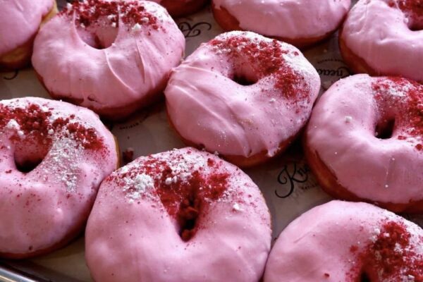 Fresh pink glazed donuts topped with red sprinkles, perfect for a sweet treat.
