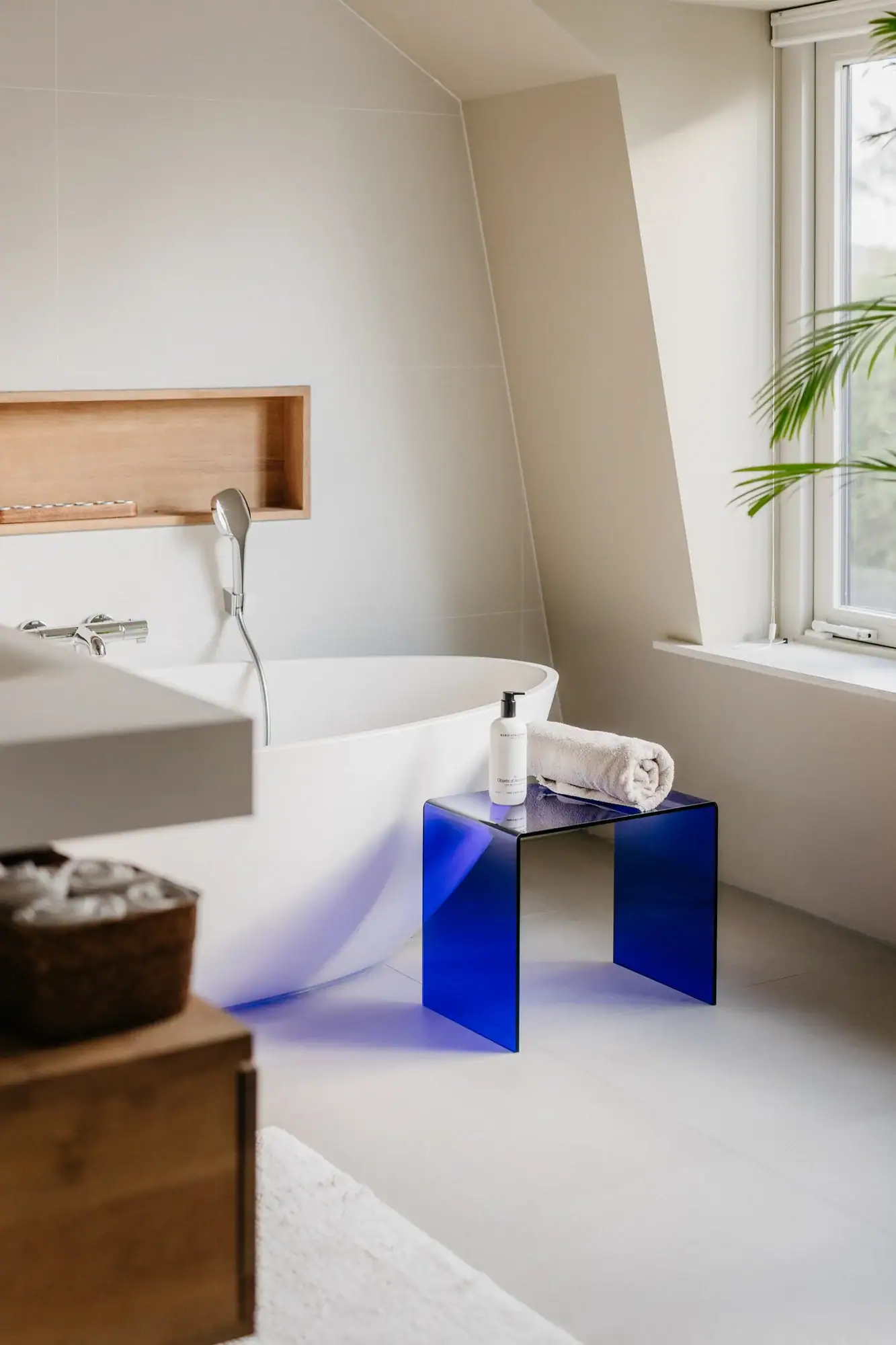 Moderne blauwe bijzettafel 'Iconic Deep' naast bad in lichte badkamer.