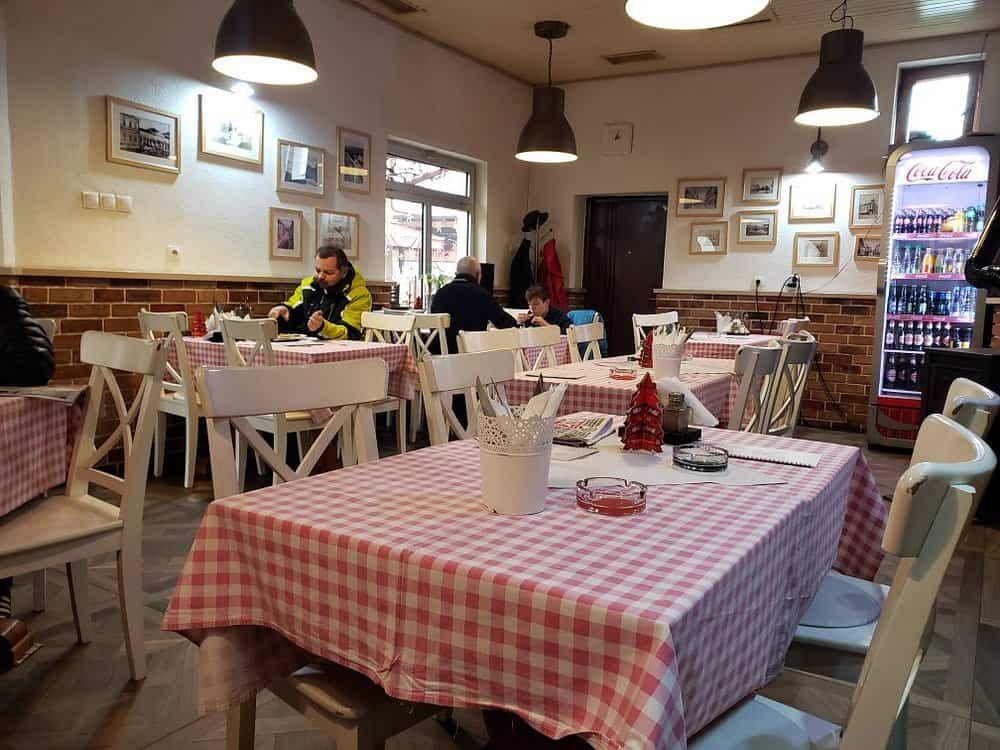 Unutrašnjost Ćevapdžinice Kod Muje sa prijatnim ambijentom, tradicionalnim stolnjacima i gostima koji uživaju u obroku.