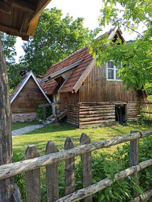 Drveni bungalov Cozy Una u Kulen Vakufu, okružen zelenilom i tradicionalnim ograđenim dvorištem.