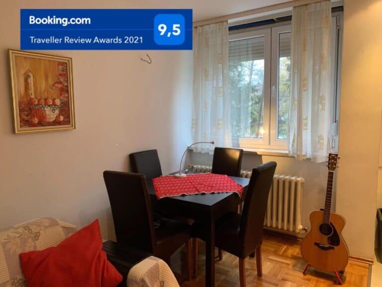 Moderno uređena dnevna soba s drvenim stolom, stolicama i akustičnom gitarom, dio Apartmana Olivia u Banjoj Luci.