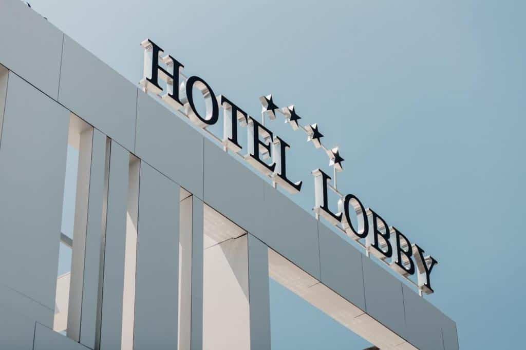 Natpis HOTELA LOBBY sa četiri zvjezdice na modernoj bijeloj fasadi, snimljen iz donjeg ugla pod plavim nebom.