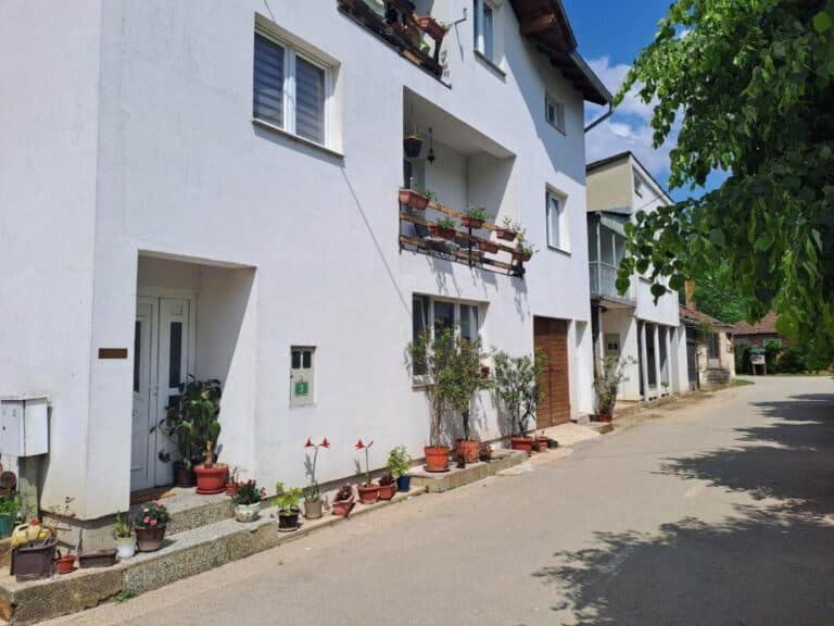 Ulaz u Apartman Naza Kulen Vakuf s bijelom fasadom, ukrašen biljkama i cvjetnim saksijama.