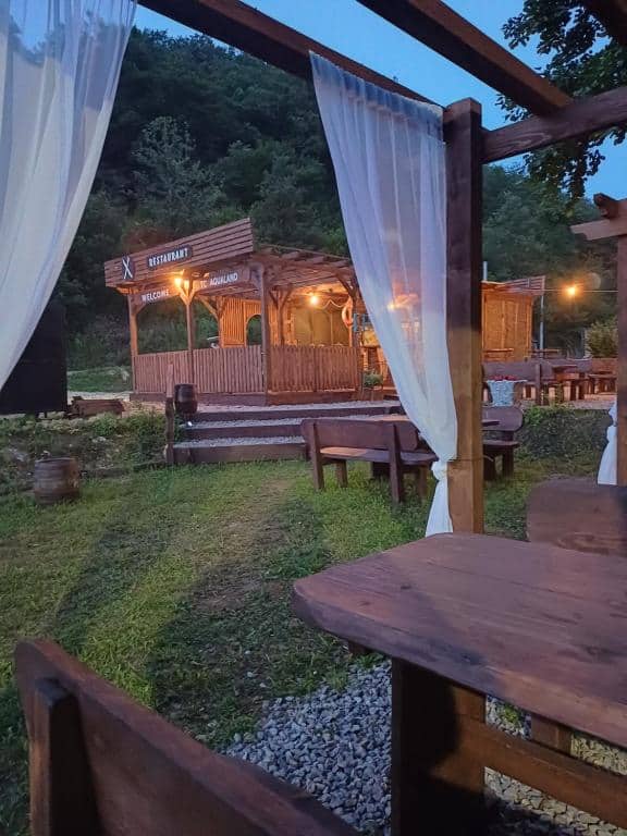 Vanjski pogled na AutoCamp Aqualand Bihać s rustikalnim drvenim stolovima i restoranom u prirodnom okruženju Nacionalnog parka Una.