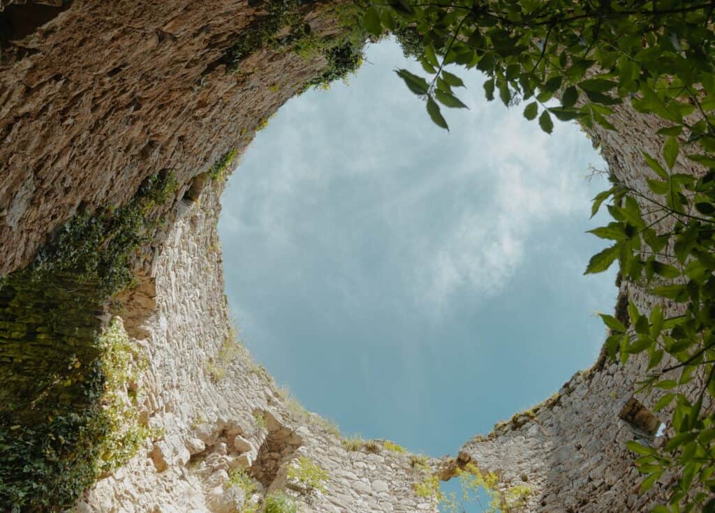 Pogled prema nebu kroz unutrašnjost Kule Radetina u Cazinu, stara kamena kula prekrivena zelenilom.