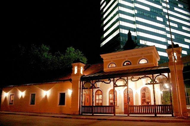 Restoran Mala Stanica u večernjem ambijentu, elegantna zgrada osvijetljena noću, s modernim neboderom u pozadini.
