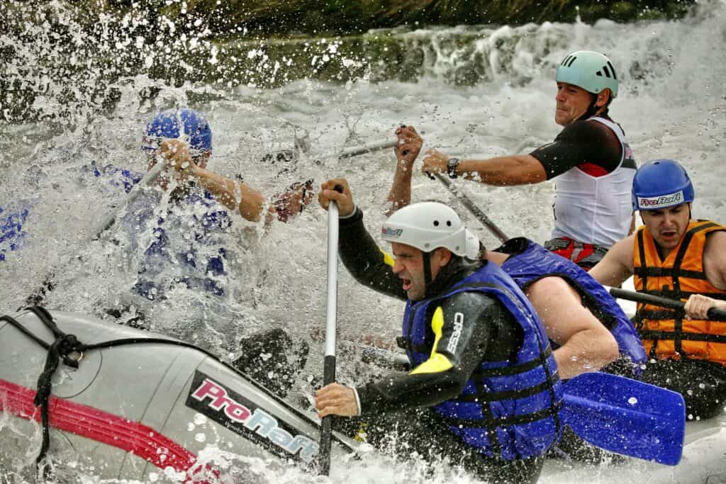 Ekipa u čamcu tokom rafting avanture na rijeci Uni, prekrivena prskanjem vode dok savladavaju brzake.
