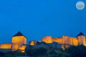 Tvrđava Tešanj noću osvijetljena toplim svjetlima, ističe svoju impozantnu arhitekturu na brdu ispod tamnog neba.