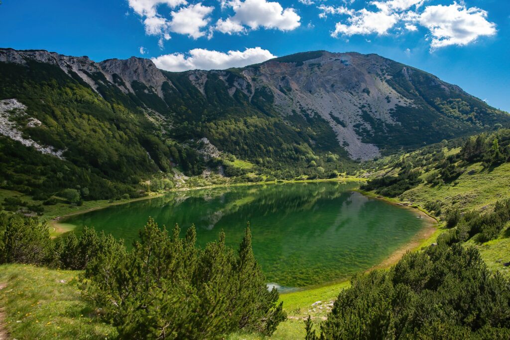 Pogled na Šatorsko jezero smješteno u planinskom okruženju, okruženo bujnim zelenilom i plavim nebom.