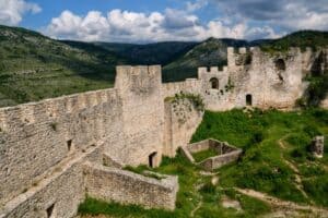"Tvrđava Blagaj iznad izvora Bune, okružena planinskim pejzažima."